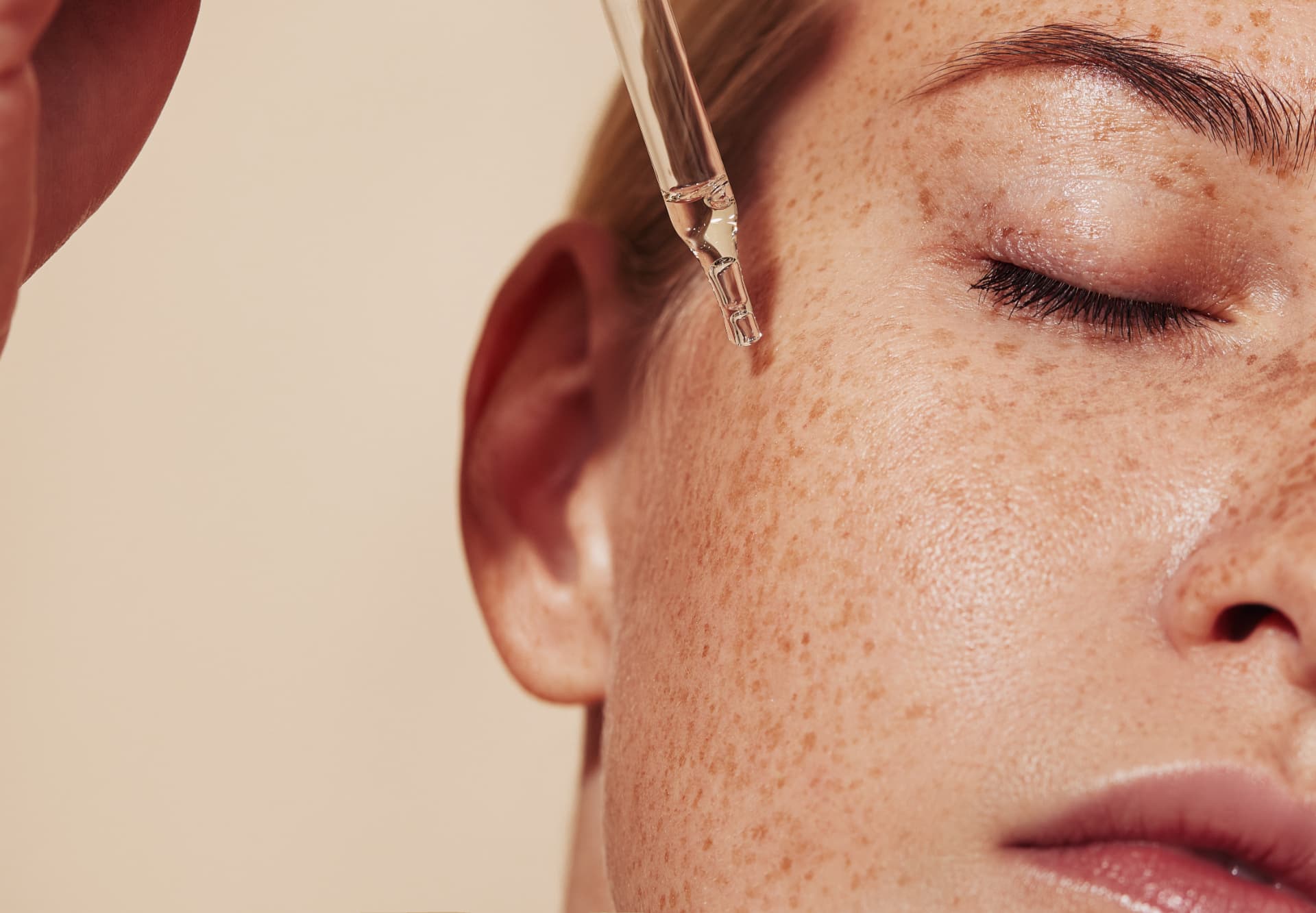 Close portrait of freckled, dewy skin with a serum dropper in warm natural light